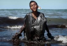 Foto de menino saindo do mar coberto por óleo roda o mundo como símbolo do desastre