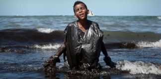 Foto de menino saindo do mar coberto por óleo roda o mundo como símbolo do desastre