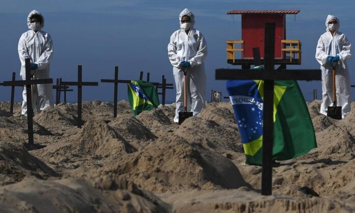 Ativistas da ONG Rio de Paz posam ao lado de cem buracos na areia da Praia de Copacabana, simbolizando sepulturas das vítimas da Covid-19 Foto: CARL DE SOUZA/AFP/11-6-2020